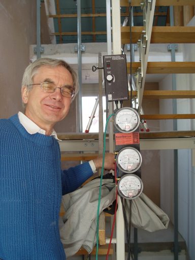 Mann mit Brille steht neben einer Messvorrichtung an einer Treppe.